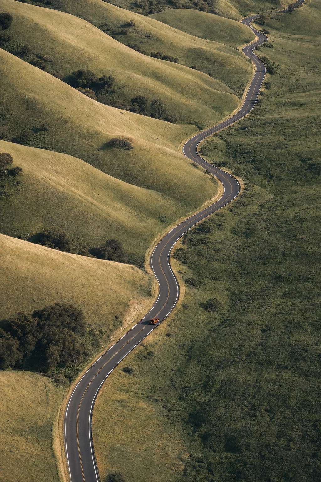 An orange car on an open road winding through California hills